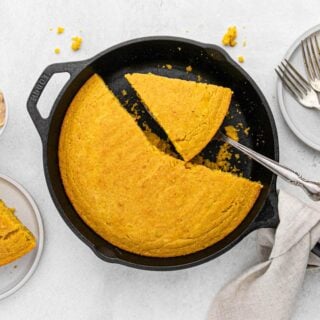 A cast iron skillet filled with pumpkin cornbread that is sliced and some pieces are missing.