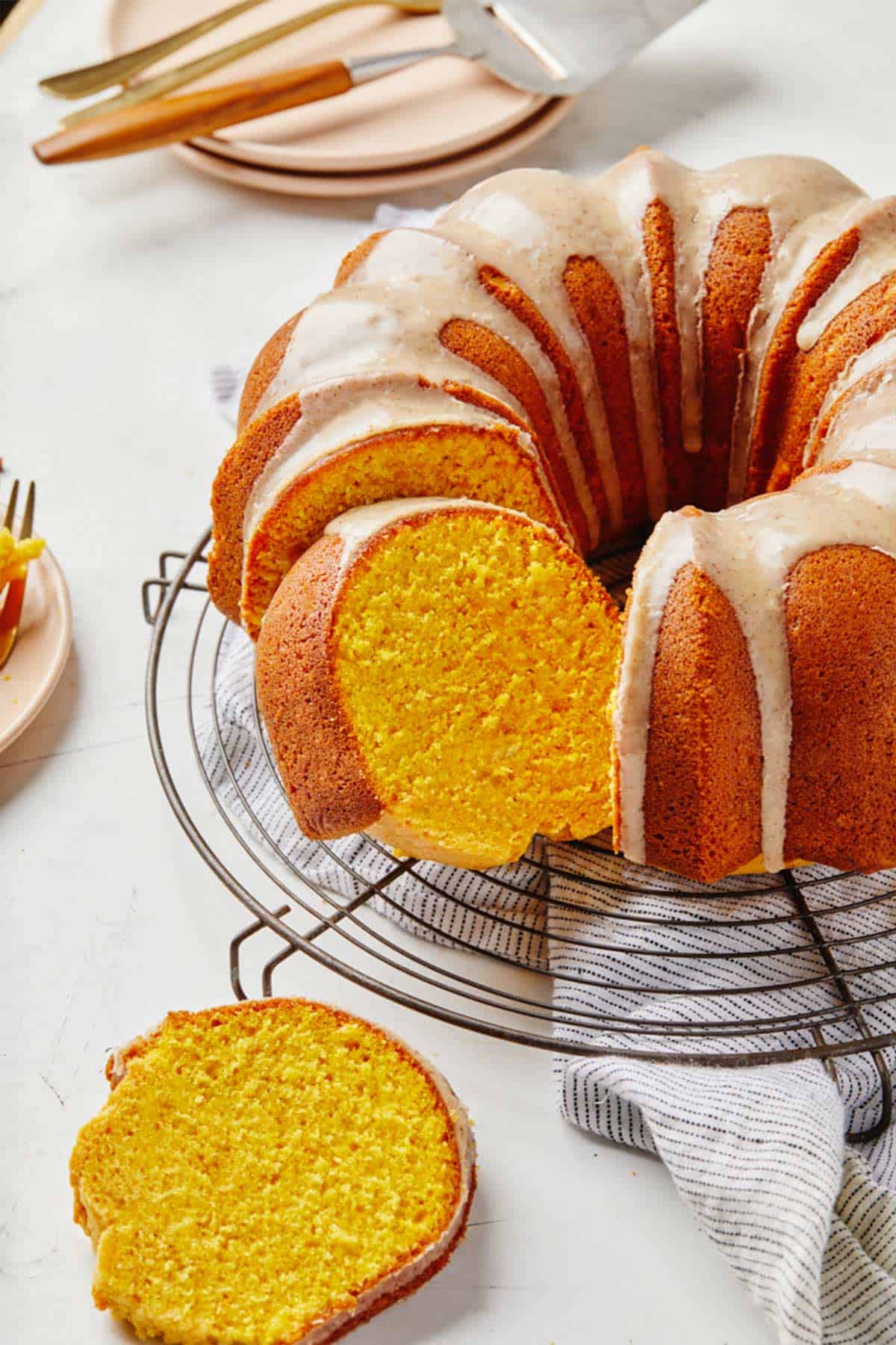 A pumpkin bundt cake with icing on a wire rack with slices cut and pulled out of the cake.