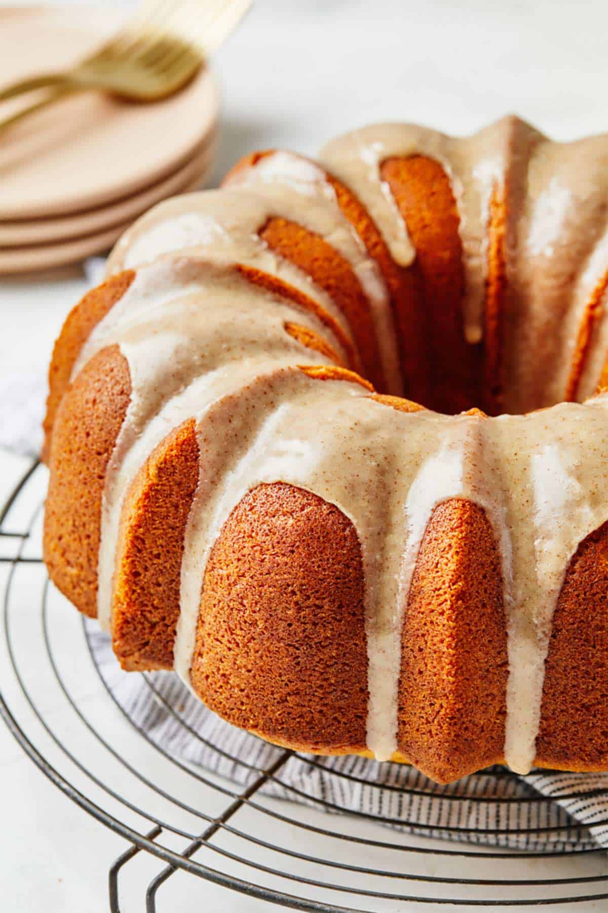 A pumpkin bundt cake on a wire rack on the table with a stack of plates in the background.