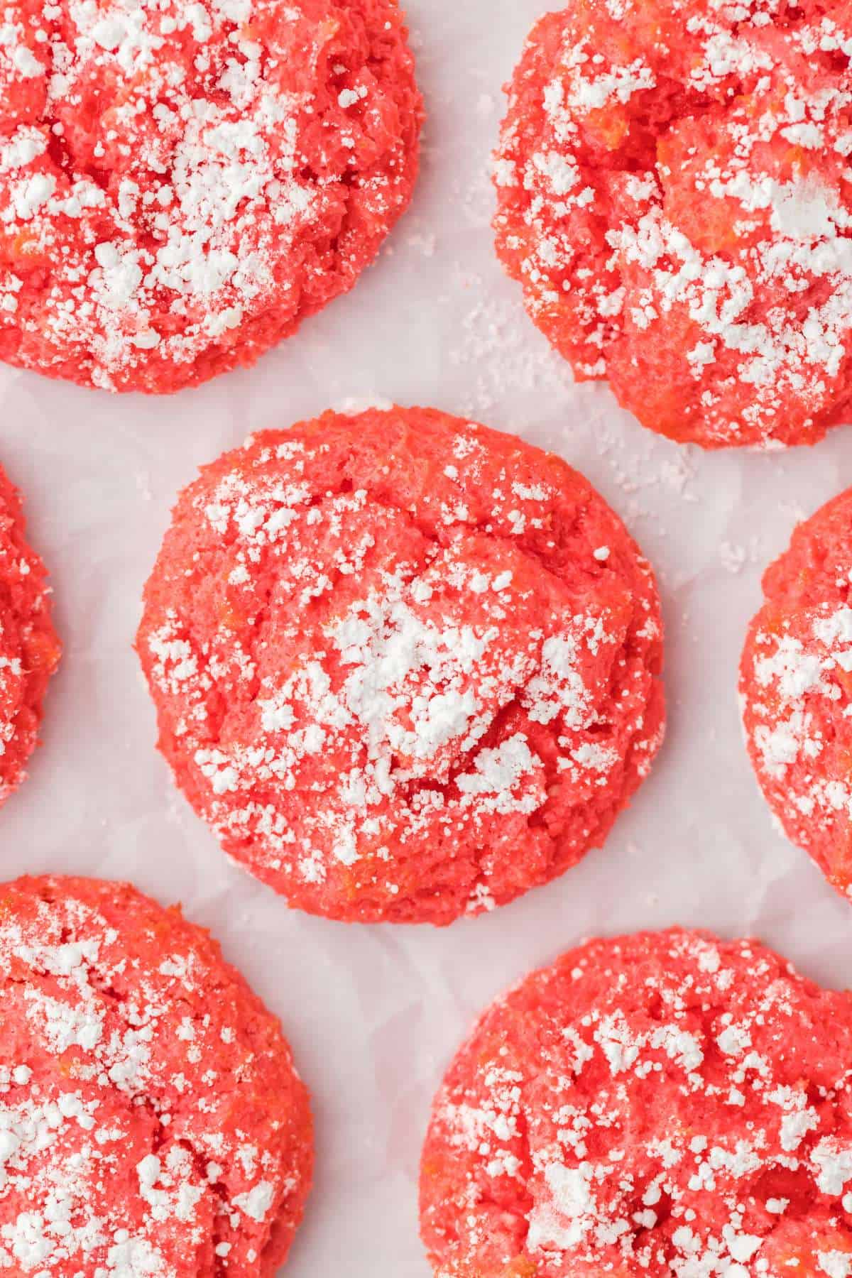 Raspberry cookies dusted with powdered sugar and laying on white parchment paper.