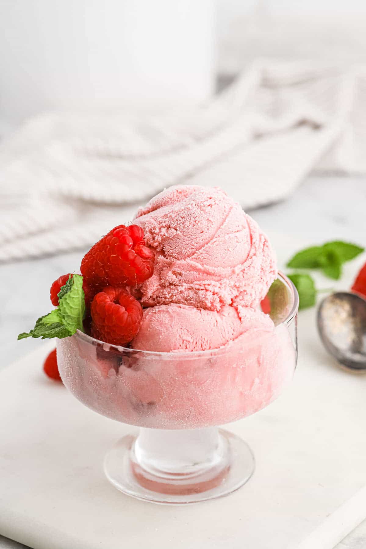 Raspberry ice cream scooped into a glass dessert cup and topped with fresh raspberries.