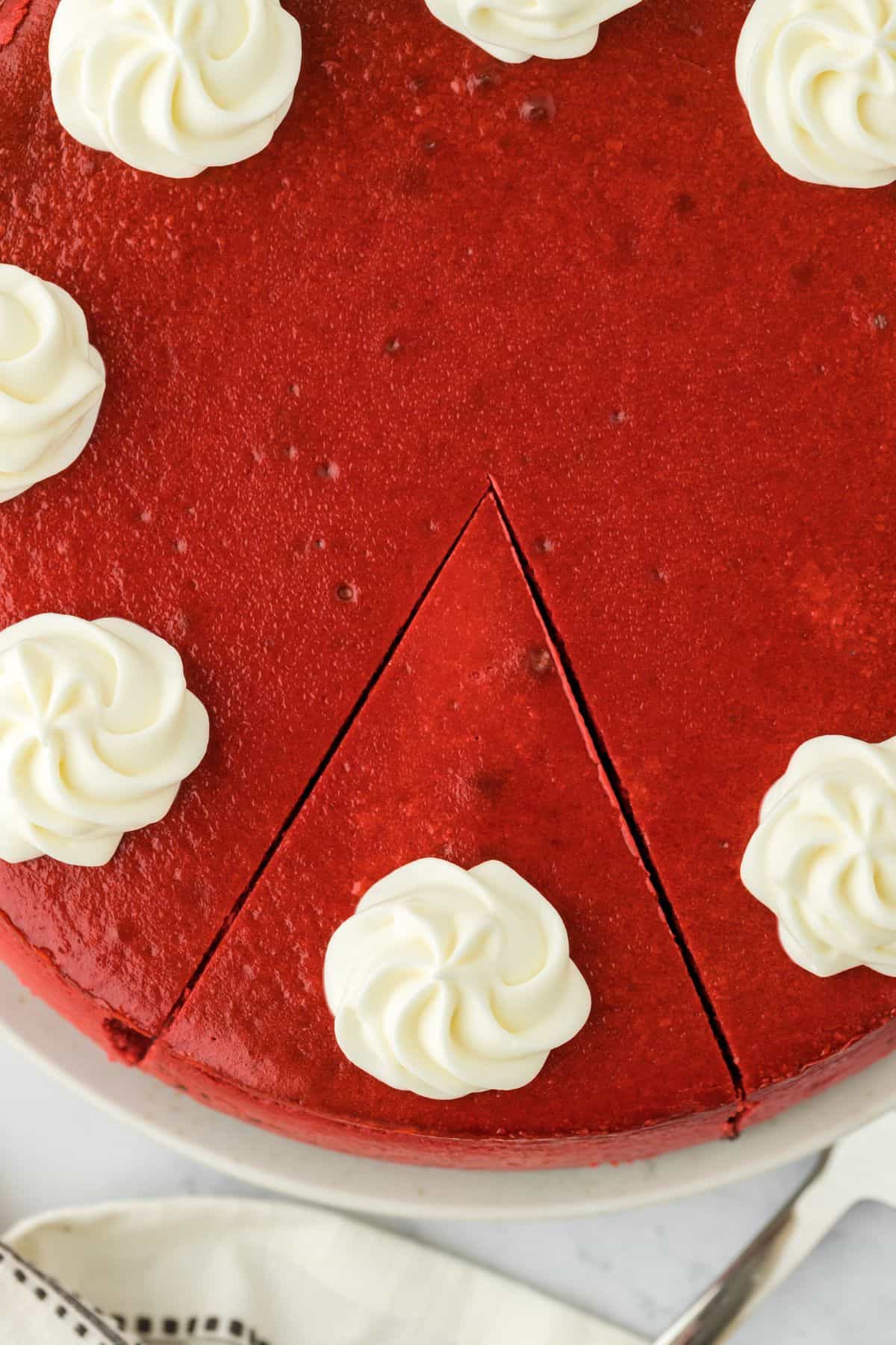 A red velvet cheesecake with a slice cut but not removed from the cheesecake.