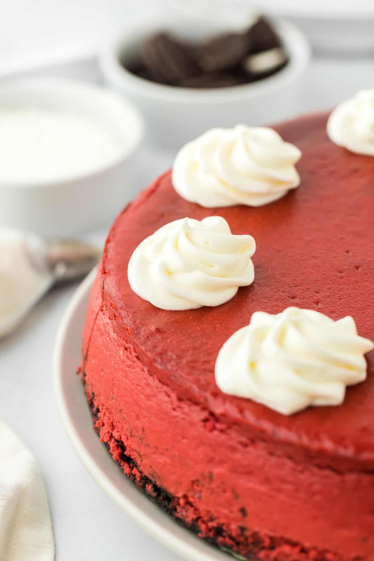 Red velvet cheesecake topped with whipped cream rosettes on a plate only showing half of it. 