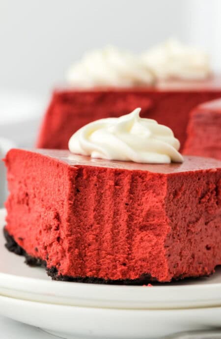 A slice of red velvet cheesecake on a plate with a bite missing.