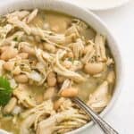 A bowl of slow cooker white chicken chili on the table with a spoon in the bowl.