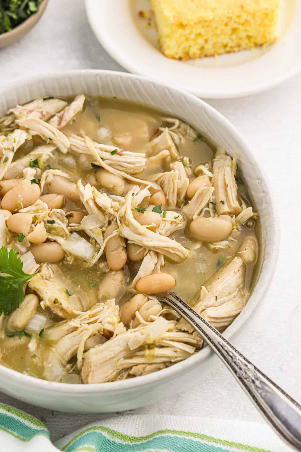 A bowl of slow cooker white chicken chili on the table with a spoon in the bowl.