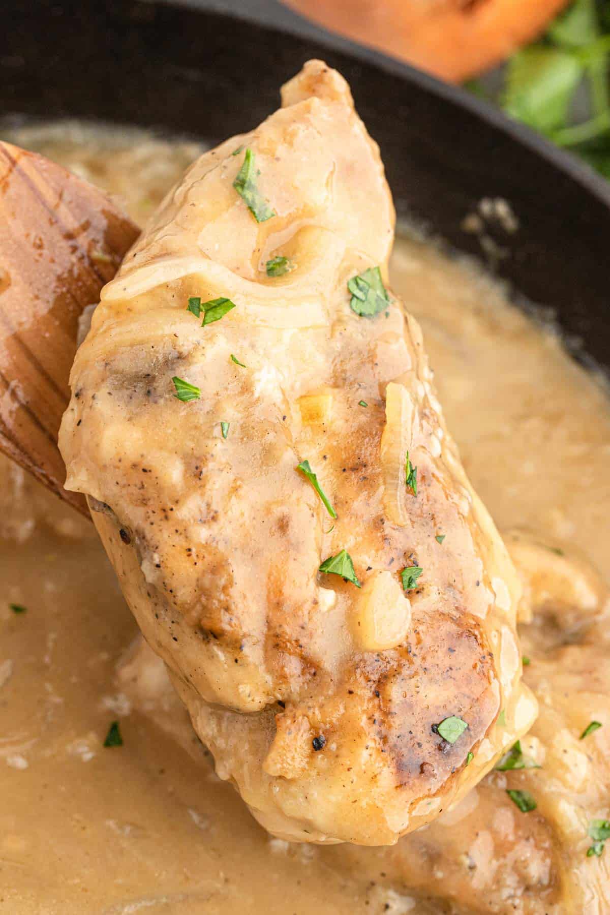 A spoon lifting a piece of smothered chicken from the skillet with homemade gravy.