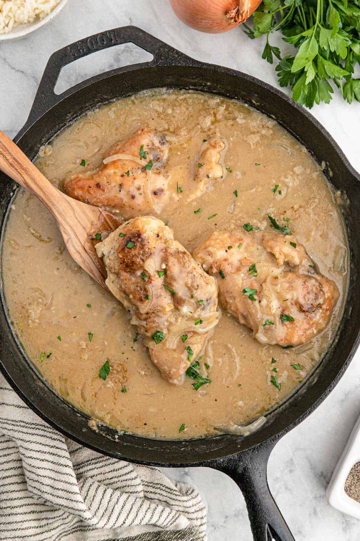 Southern smothered chicken in a cast iron skillet with a wooden spoon.