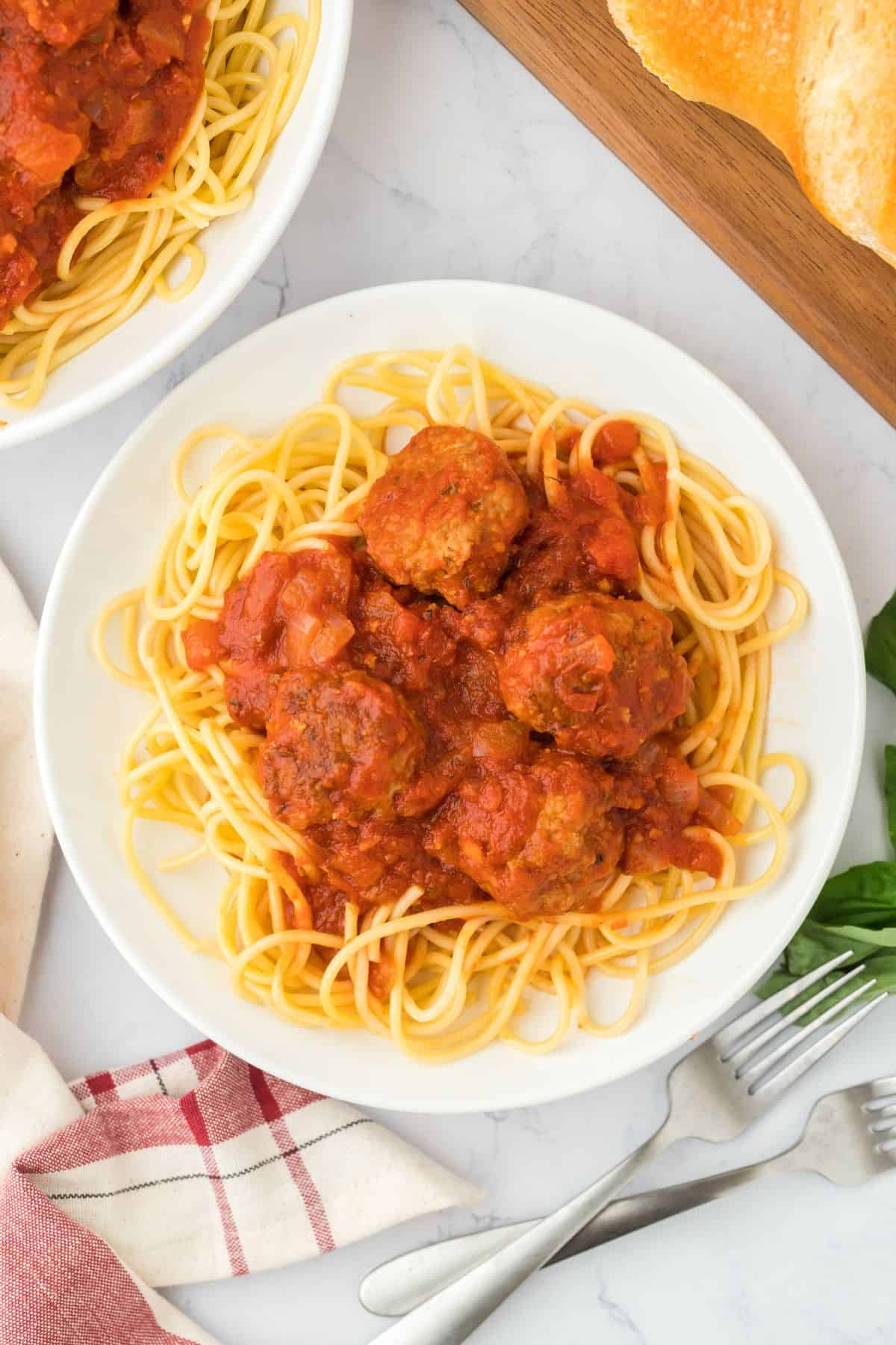 A plate of soul food spaghetti and meatballs on a white plate with a another serving bowl in the corner and a loaf of bread.