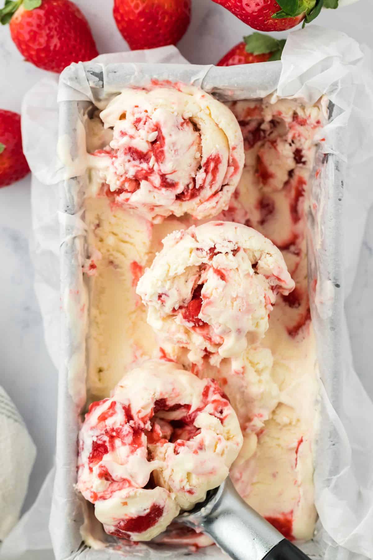 Strawberry Cheesecake Ice Cream in a loaf pan with scoops of ice cream on top and strawberries around the pan.