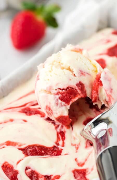 Strawberry Cheesecake Ice Cream in a container with a scoop on top filled with a scoop of ice cream.