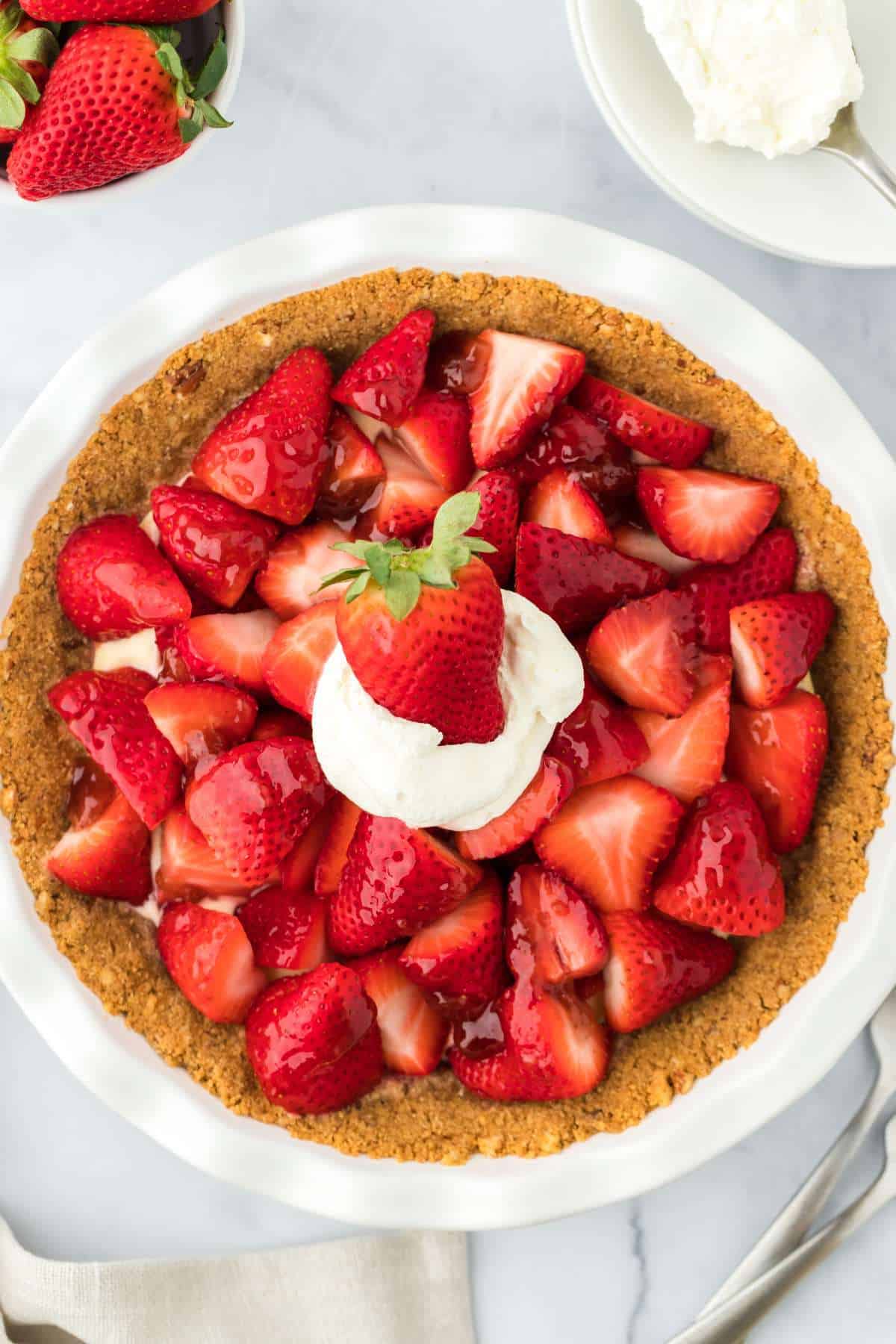 A strawberry custard pie topped with fresh whole strawberries and whipped cream