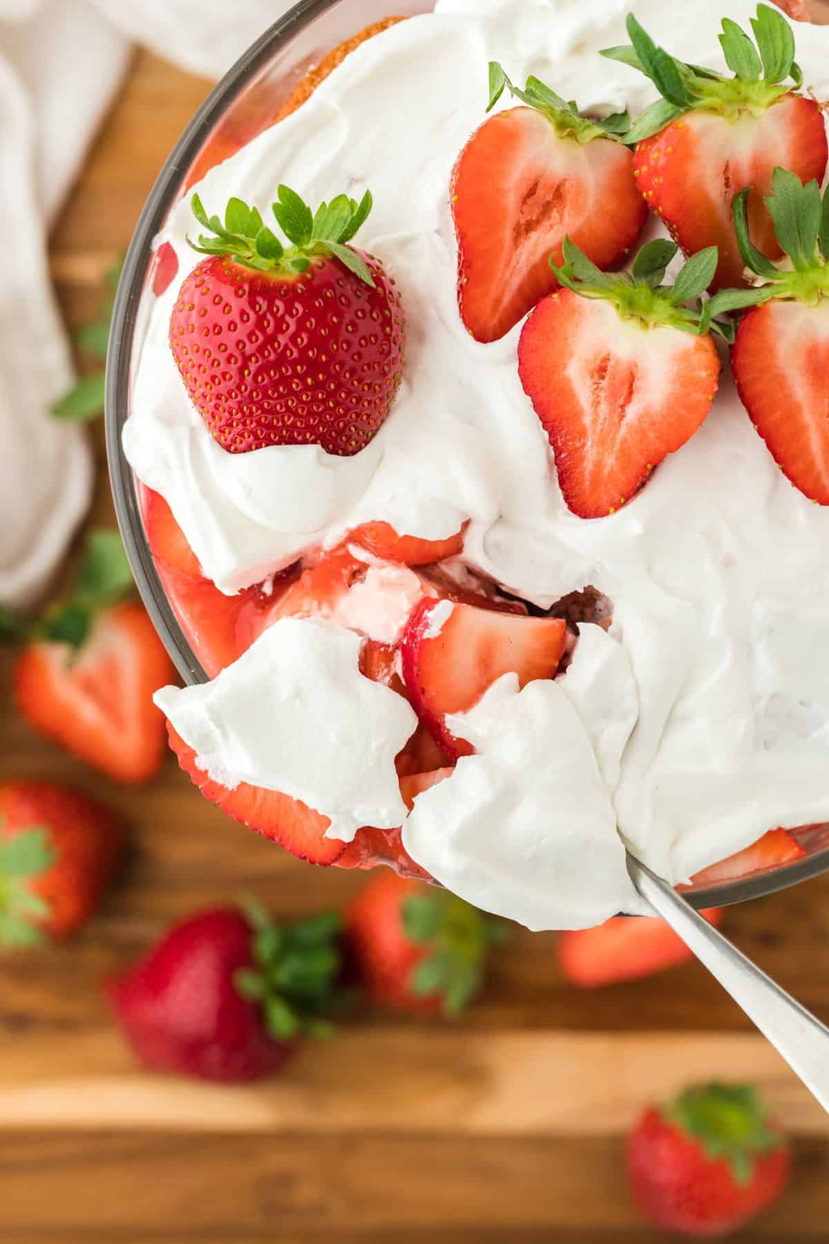 A strawberry shortcake trifle with a basket of fresh strawberries in the background.