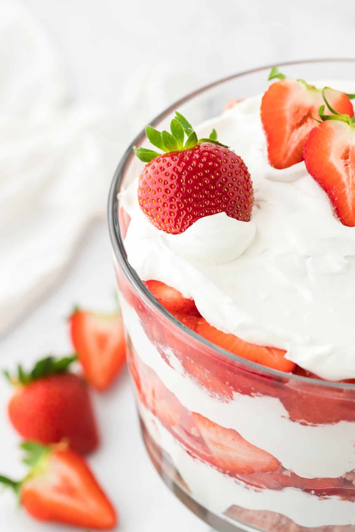 A half of a strawberry shortcake trifle on the table with some strawberries cut in half and whole to the side.