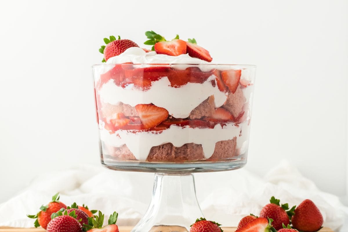 A strawberry trifle on the table with white napkin in the background and strawberries surrounding the base of the dish. 