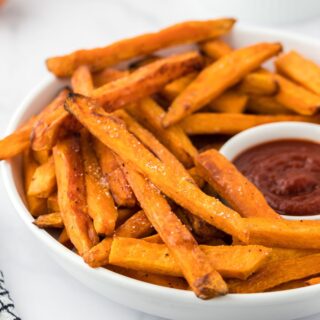 A bowl of sweet potato fries with ketchup on the table ready to eat.