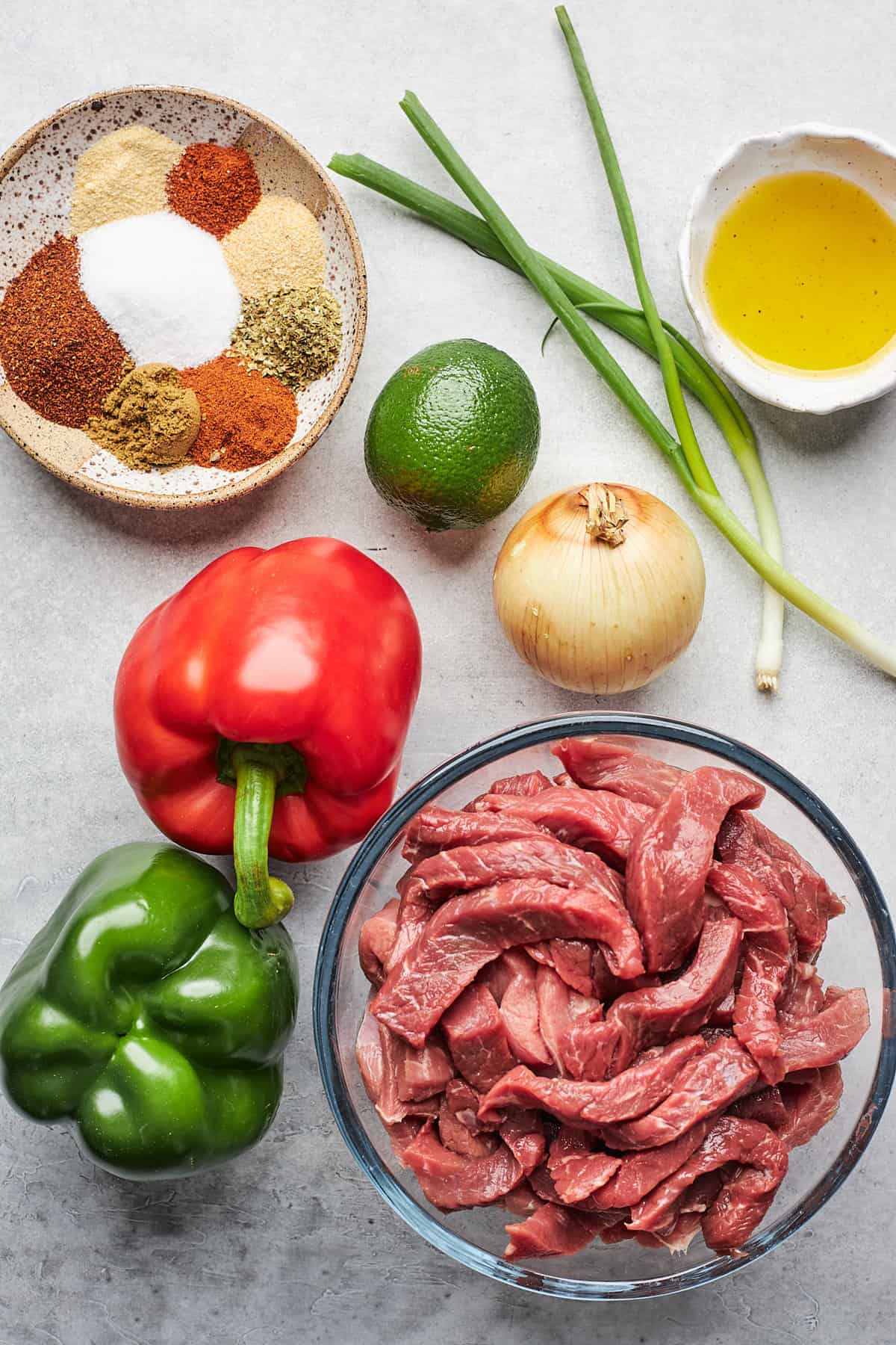 Sliced steak, peppers, onions and seasonings in bowls