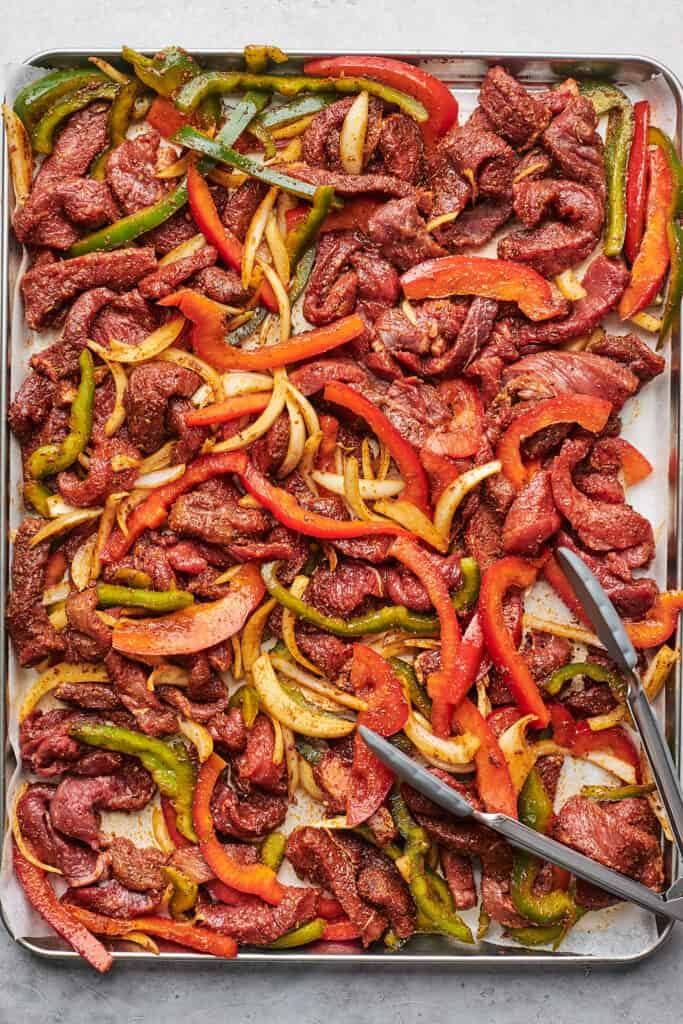 Steak fajitas spread on a sheet pan before baking