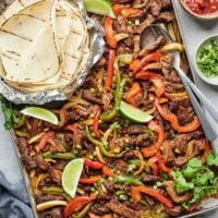 Sheet-pan steak fajitas with garnishes and tortillas to serve with