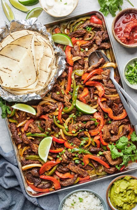 Sheet-pan steak fajitas with garnishes and tortillas to serve with