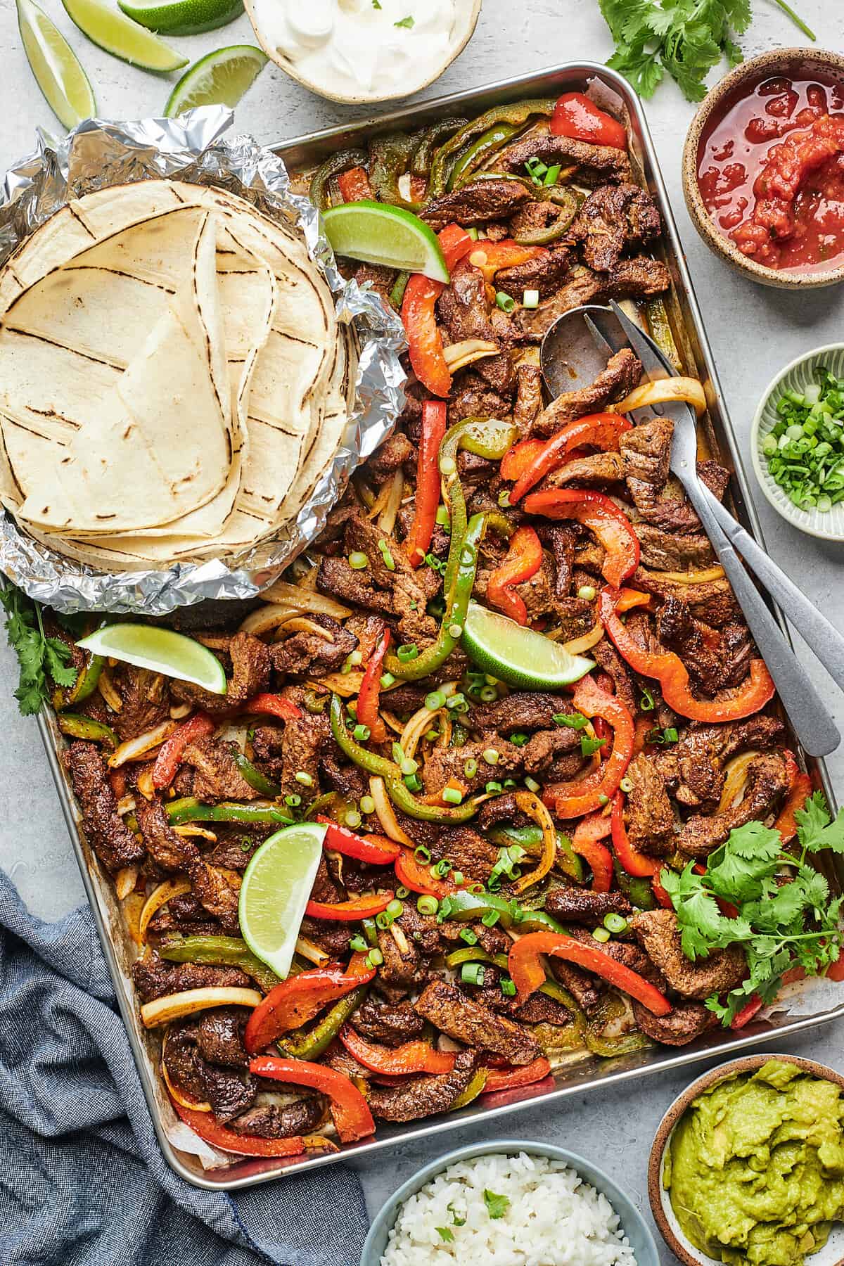 Sheet-pan steak fajitas with garnishes and tortillas to serve with