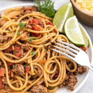 Completed dish of taco spaghetti garnished with lime wedges.