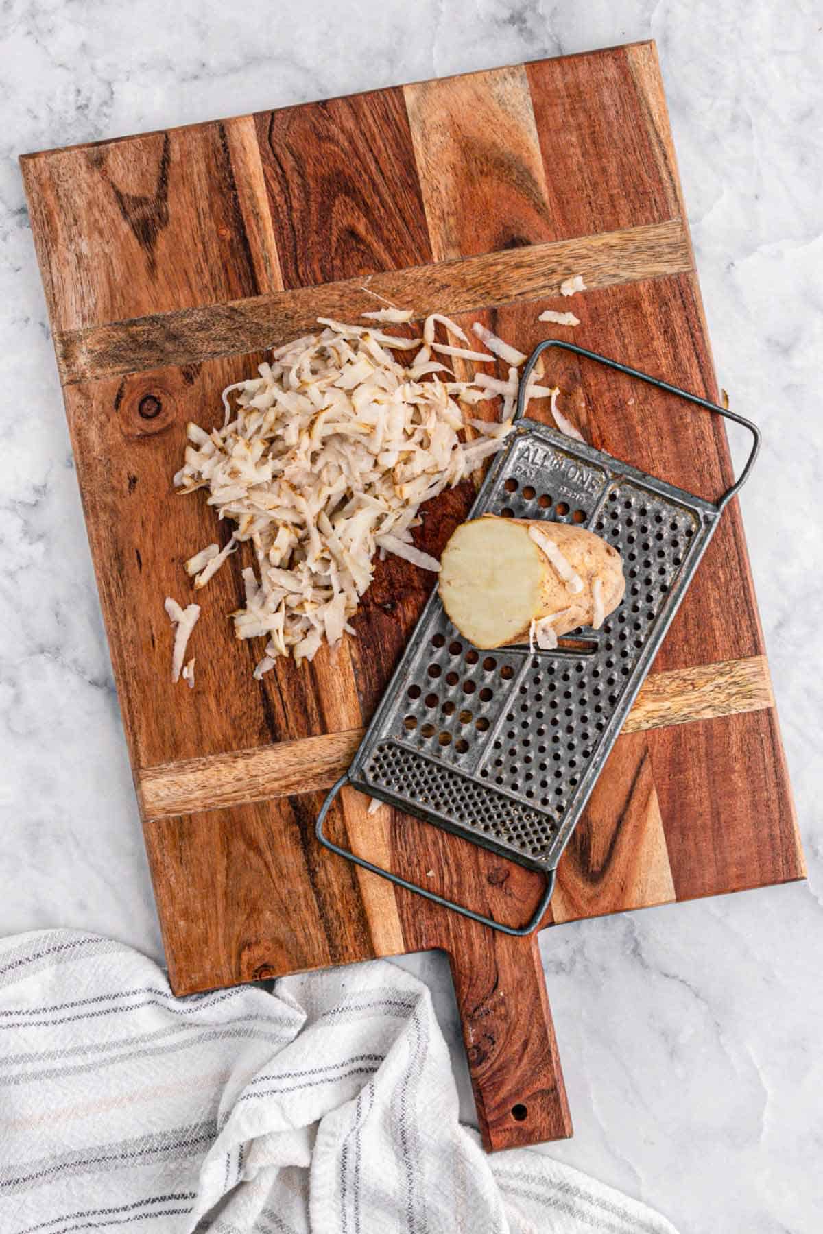 Potatoes shredded on a cutting board with a cheese grater next to it.