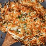Cooked hash browns in a skillet with a wooden spoon under the potatoes in the pan.