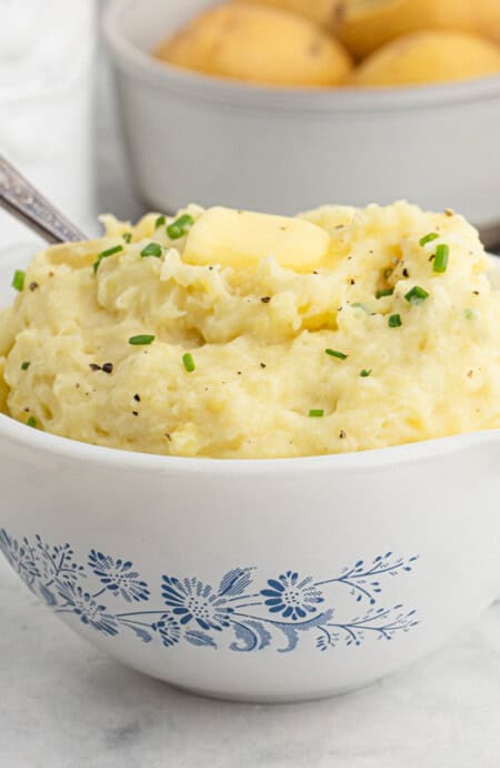 A serving bowl full of slow cooker buttermilk mashed potatoes with a spoon.