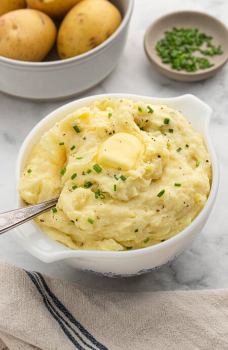 A serving bowl full of slow cooker buttermilk mashed potatoes with a spoon.