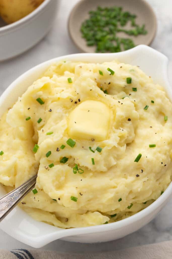 A serving bowl full of slow cooker buttermilk mashed potatoes with a spoon.