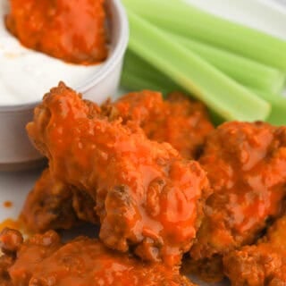 Buffalo wings on a plate with celery and one being dipped in ranch
