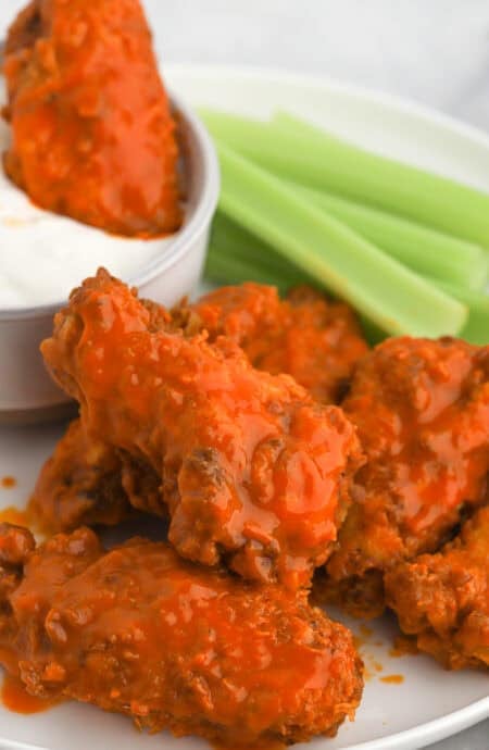 Buffalo wings on a plate with celery and one being dipped in ranch