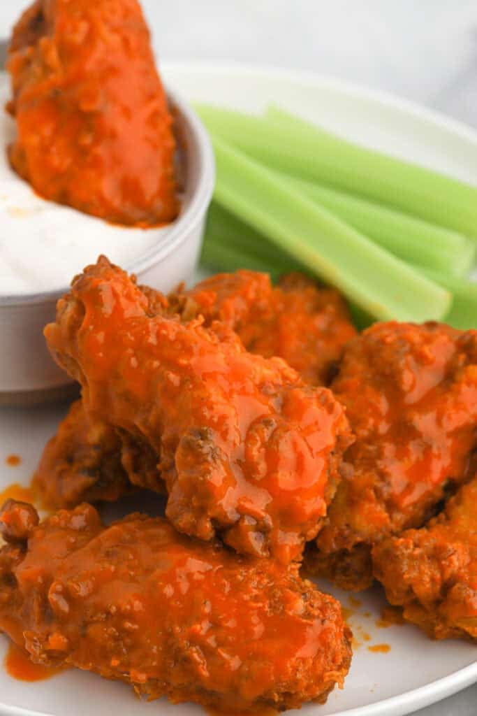 Buffalo wings on a plate with celery and one being dipped in ranch
