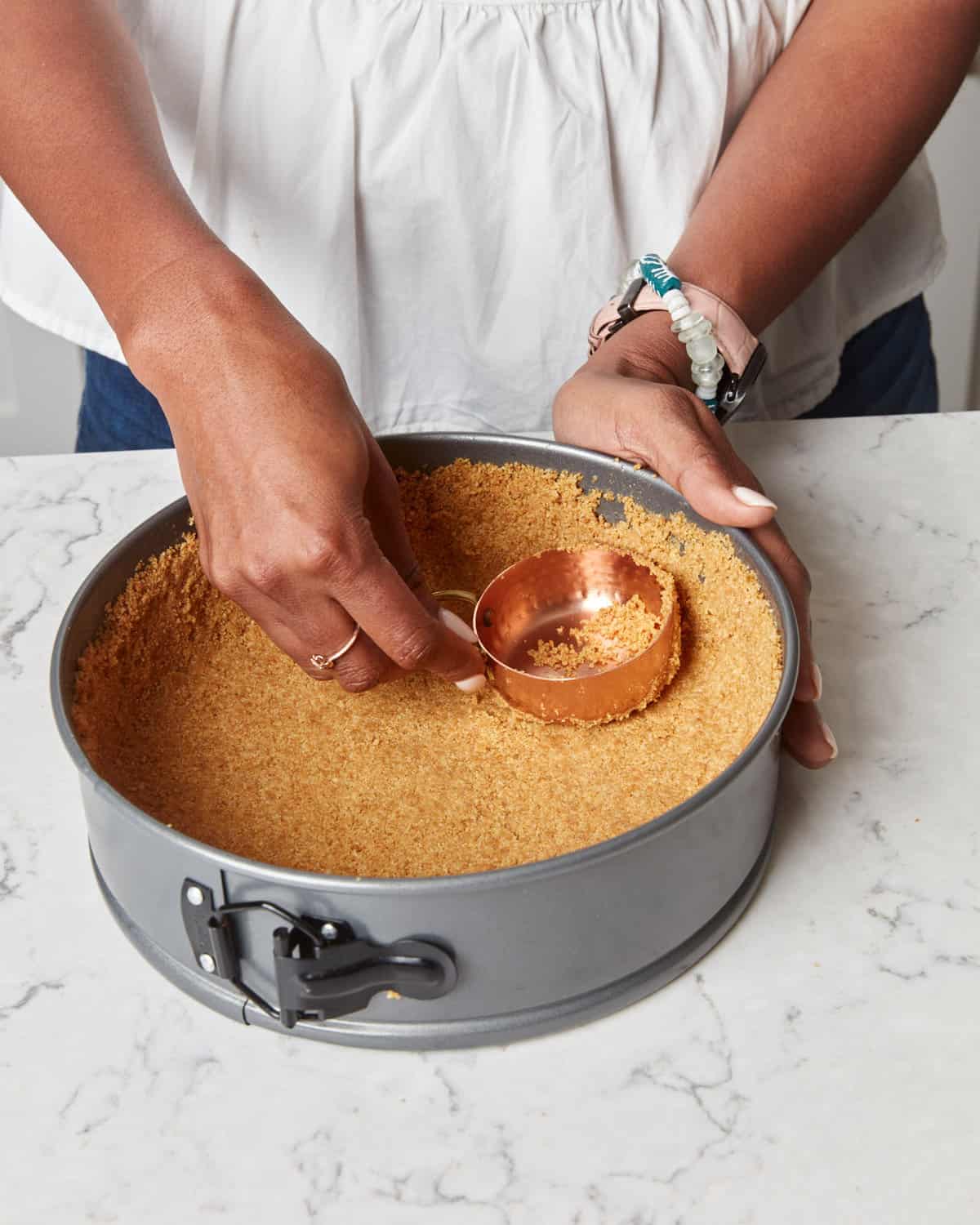 Pressing graham crumb crust into a springform pan.