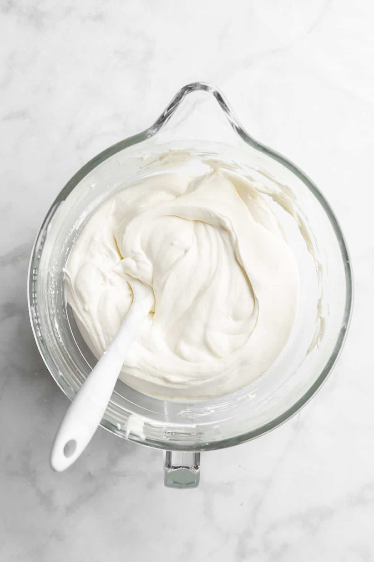 Whipped cream in the glass bowl of a stand mixer.