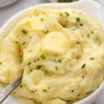 A serving bowl full of slow cooker buttermilk mashed potatoes with a spoon.
