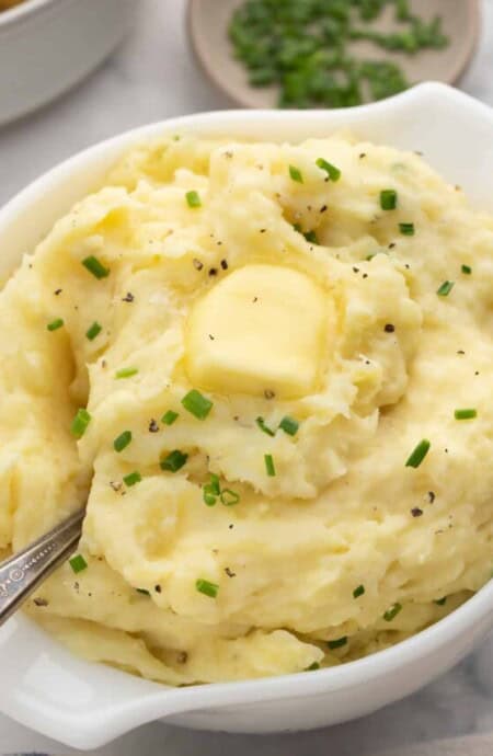 A serving bowl full of slow cooker buttermilk mashed potatoes with a spoon.