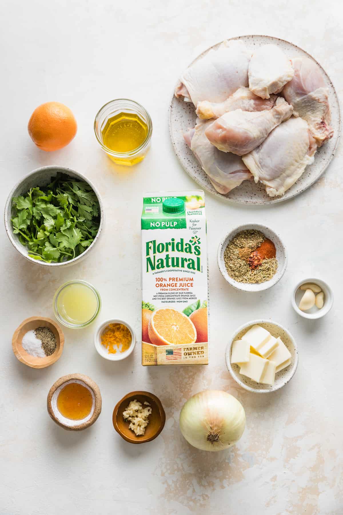 Ingredients to make baked orange herb chicken on a white surface.
