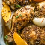 Closeup of herbed chicken pieces in a dish with oranges and onions.