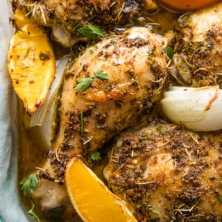 Closeup of herbed chicken pieces in a dish with oranges and onions.