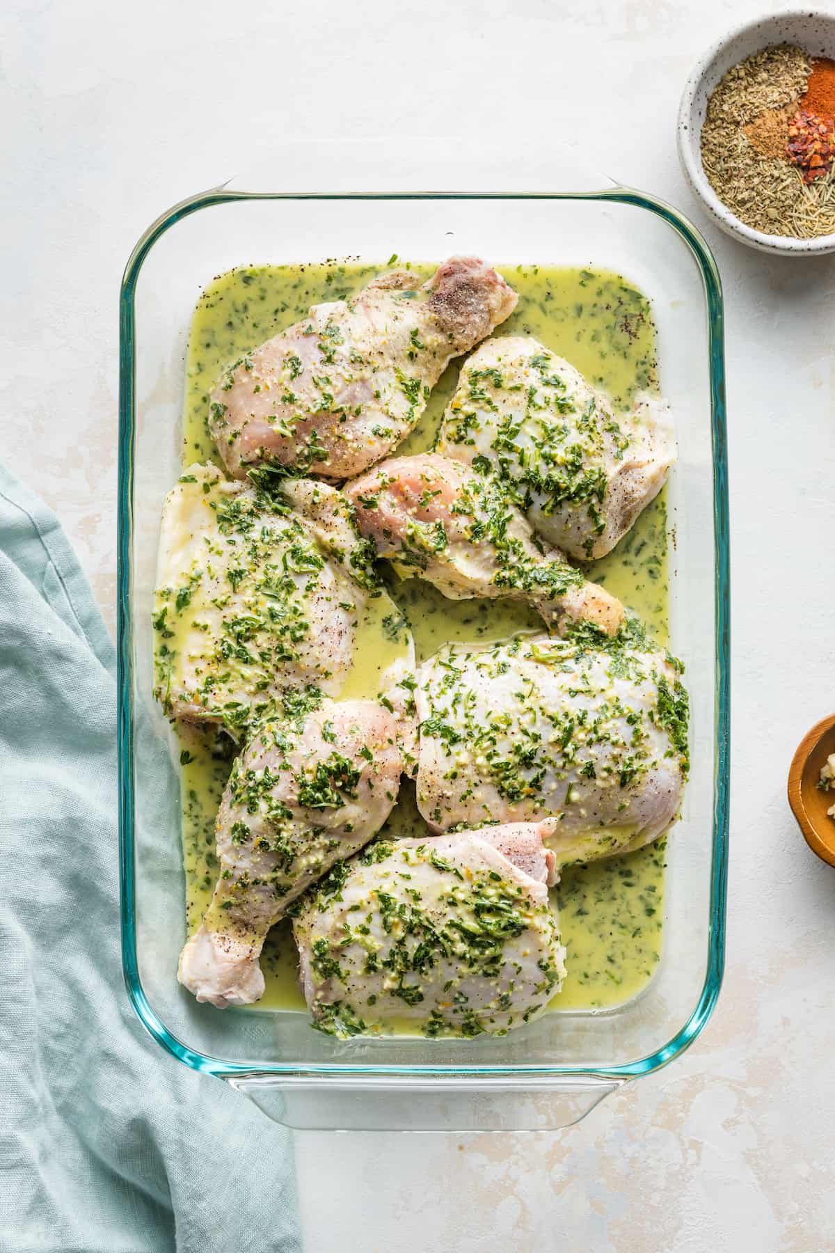 Orange herb sauce poured over raw chicken pieces in a baking dish.