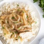 Overhead shot of a white plate with a serving of Southern smothered chicken over rice, with a piece of chicken cut open to show the white meat, and a fork beside it