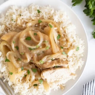 Overhead shot of a white plate with a serving of Southern smothered chicken over rice, with a piece of chicken cut open to show the white meat, and a fork beside it