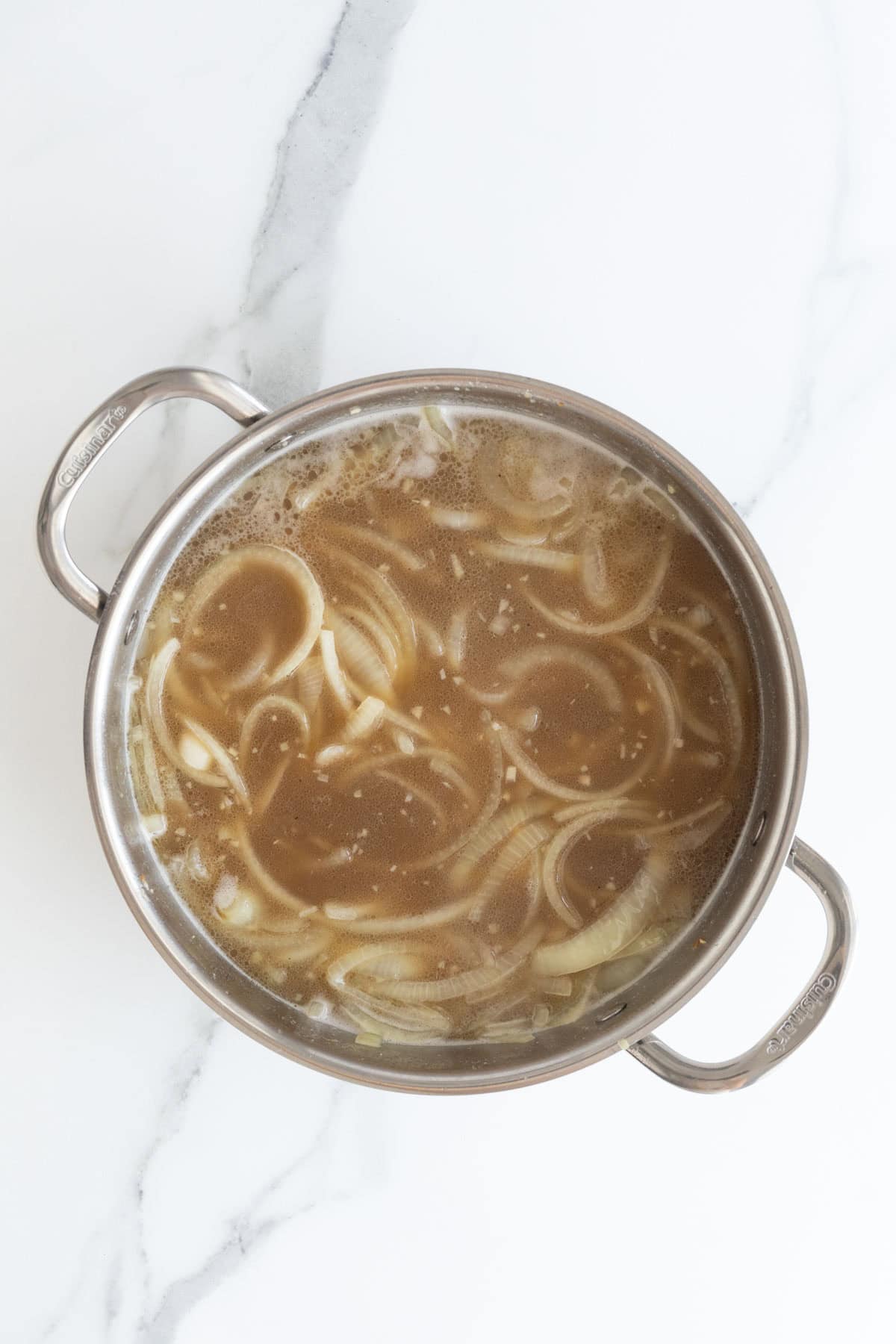 Sliced onions in a darker, richer broth in a stainless steel pot