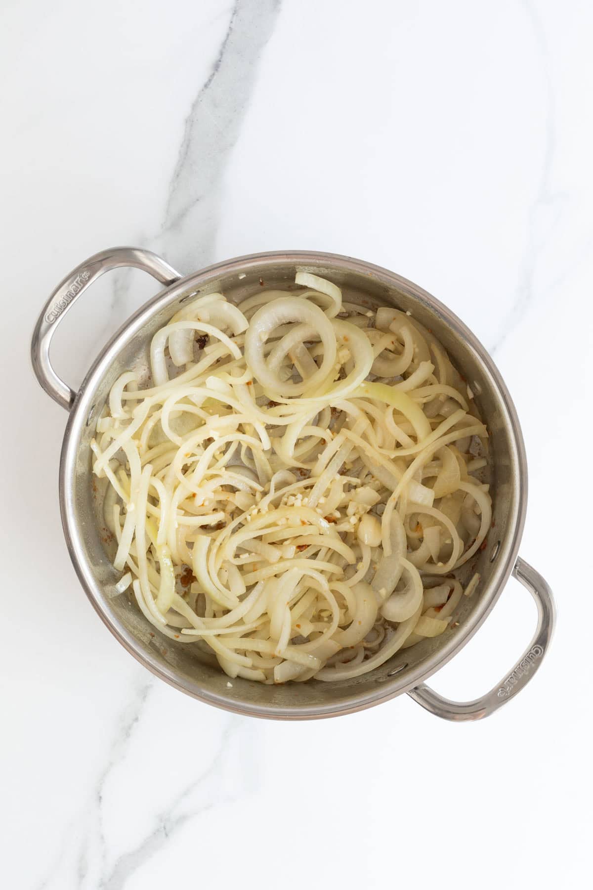 Sliced onions and minced garlic sauteing in a stainless steel pot