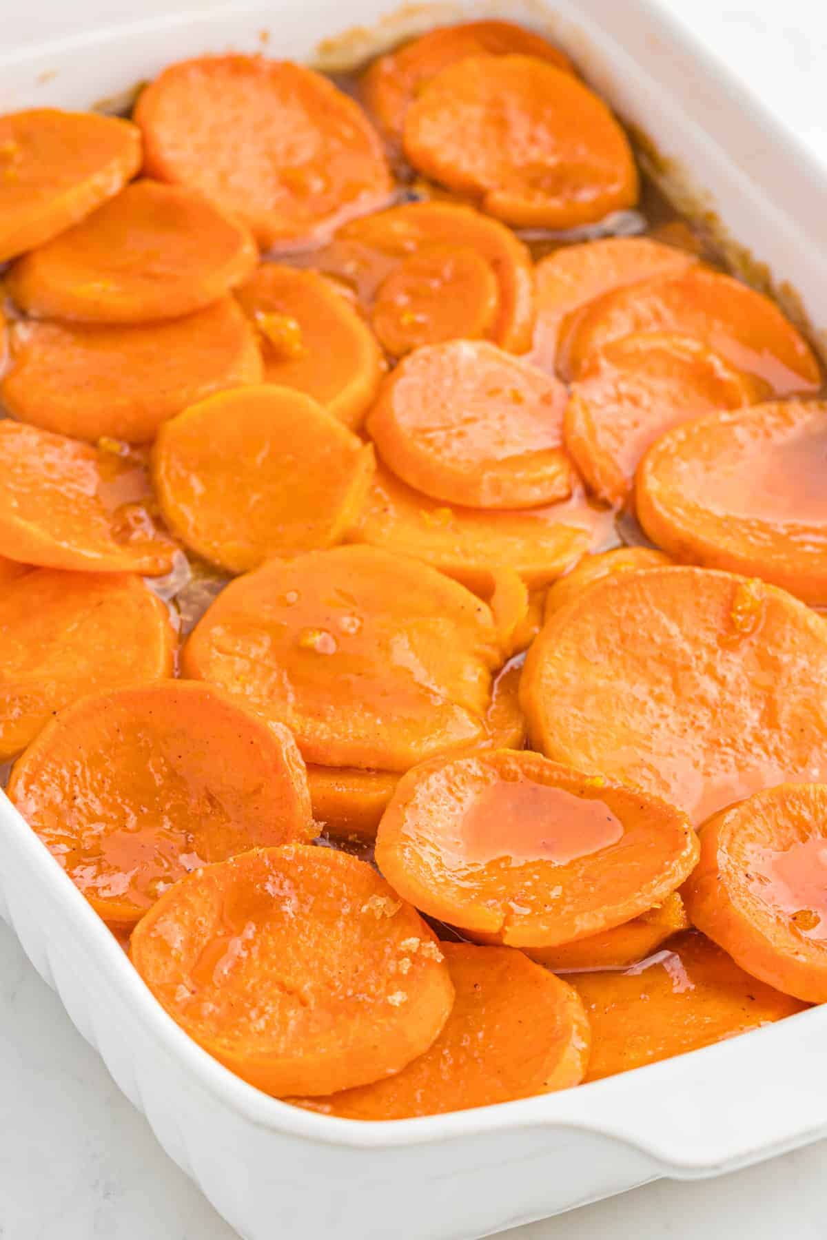 A white baking dish of sliced candied yams in syrup