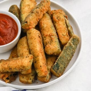 Air fried zucchini plated with dipping sauce.
