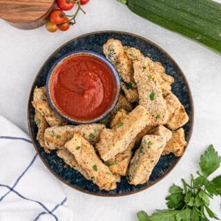 Air fried zucchini plated with dipping sauce.