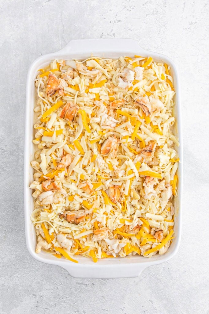 Shredded cheese over baking dish of lobster mac and cheese.
